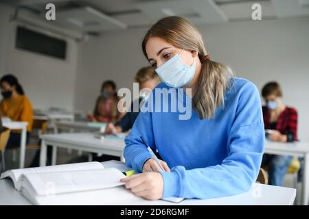 Young students with face masks at desks at college or university, coronavirus concept. Stock Photo