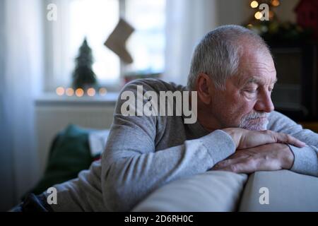 Lonely senior man sitting and sleeping on sofa indoors at Christmas, solitude concept. Stock Photo