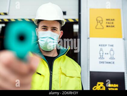 Worker with face mask in front of warehouse, coronavirus and temperature measuring concept. Stock Photo