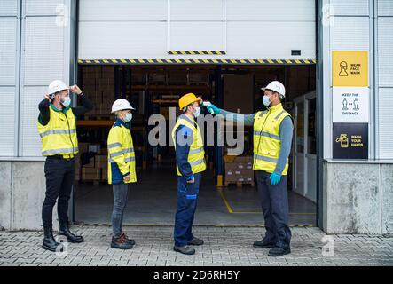 Group of workers with face mask in front of warehouse, coronavirus and temperature measuring concept. Stock Photo