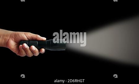Black flashlight in human hands on a black background, including a white beam. Stock Photo