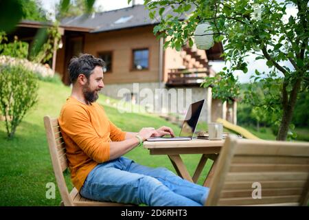 Side view of man with laptop working outdoors in garden, home office concept. Stock Photo