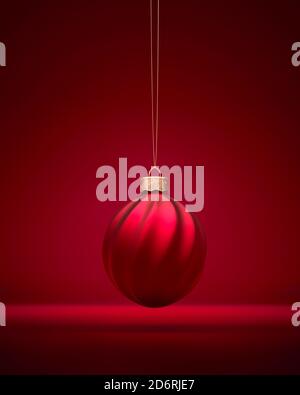 Red matt Christmas ball hanging on golden string. Christmas ornament decorated with twisted stripes. Christmas decoration, festive atmosphere concept. Stock Photo