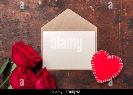 Valentines day greeting card with red roses, envelope and decorative hearts on wooden background. Top view. Copy space - Image Stock Photo