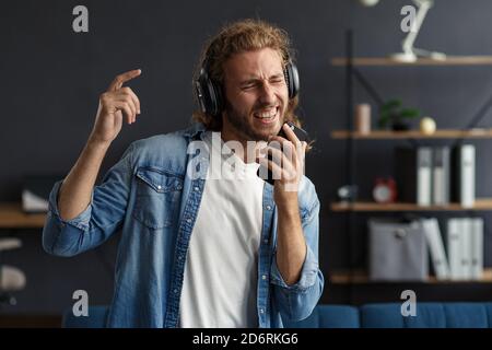 Handsome long haired curly man with headphones listening music,singing and dancing.Funny emotional smiling man with earphones and mobile phone relax Stock Photo