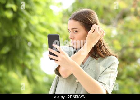Beautiful woman combing using smart phone as a mirror in a park Stock Photo
