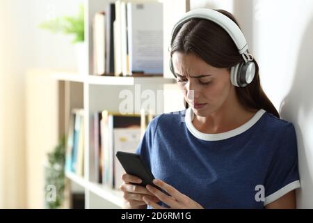 Sad teen listening to music from smart phone standing in the living room at home Stock Photo