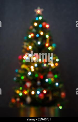 Vertical view of blurred christmas tree with garlands on gray background. Abstract backdrop with defocused lights Stock Photo