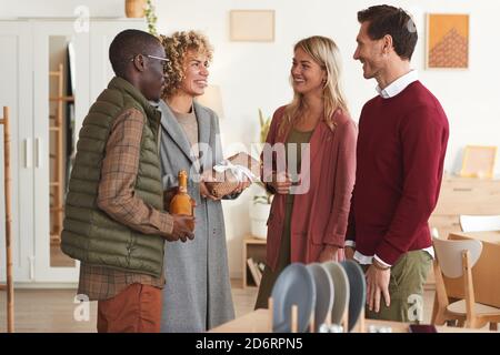 Multi-ethnic group of elegant adult people greeting each other and exchanging gifts while welcoming guests at dinner party indoors Stock Photo