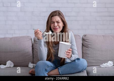 Emotional eating. Stressed woman crying on sofa with bucket of ice cream, watching sad movie and feeling depressed Stock Photo