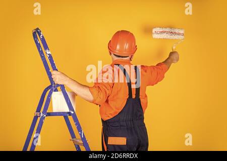 Foreman inspector. senior man painter use roller on ladder. painting the wall in yellow. professional painter in working clothes. worker painting wall in room. male decorator painting with roller. Stock Photo
