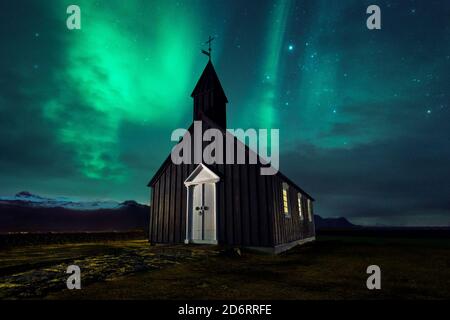 Magnificent scenery of wooden church located on meadow on background of sky with aurora borealis phenomenon in Iceland at night Stock Photo