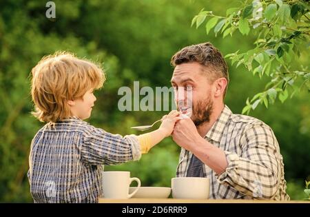 Feed your baby. Natural nutrition concept. Feeding son natural foods. Stage of development. Feed son solids. Dad and boy eat and feed each other outdoors. Ways to develop healthy eating habits. Stock Photo