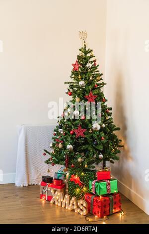 Wrapped present boxes placed under decorated Christmas tree with shiny baubles and garlands in room corner Stock Photo