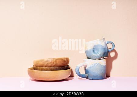 Still life with handmade ceramic cups and wooden bowls on bright studio Stock Photo