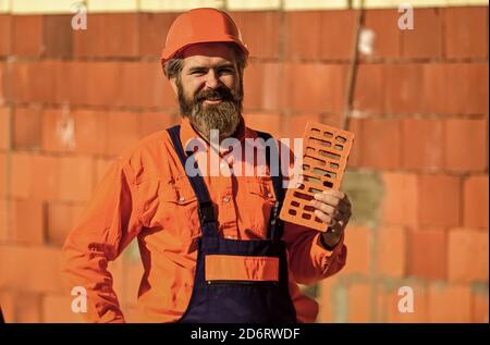 Element in masonry construction. Builder hold brick. Bearded man wear hard hat at construction site. Brick building material used to make walls. Lightweight brick made from expanded clay aggregate. Stock Photo