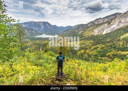 Active sporty man having a rest on the peak of Alps, Austria. Backpacker enjoying view of mountains and lake. Wanderlust freedom travel concept. Stock Photo