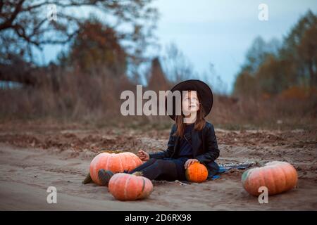 A cute girl in a Halloween costume is sitting on the road in the Park and looking at the sky. Stock Photo