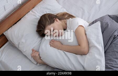 Top view of depressed young woman lying in bed and hugging her pillow Stock Photo