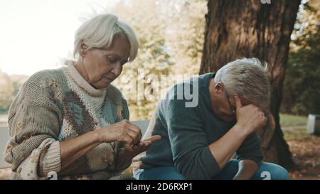 Elderly worried couple sitting on the bench in despair. Woman counting last coins. High quality photo Stock Photo