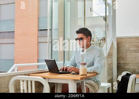 Young stylish male freelancer working remotely on laptop in cafe Stock Photo