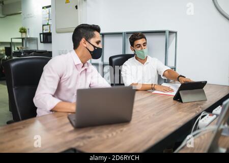 Side view of anonymous entrepreneurs in formal apparel and face masks working on project while surfing internet on netbook at office table Stock Photo
