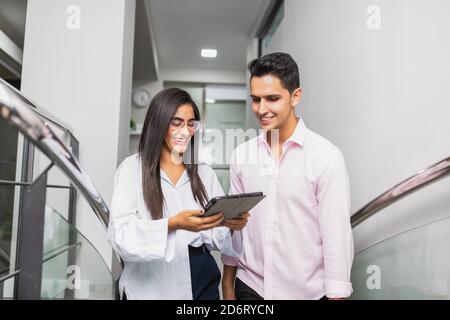 Cheerful young entrepreneurs in trendy apparel interacting while watching tablet on stairs at work Stock Photo