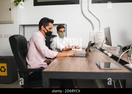 Side view of anonymous entrepreneurs in formal apparel and face masks working on project while surfing internet on netbook at office table Stock Photo