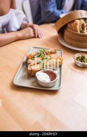 High angle of appetizing vegan stuffed spring rolls garnished with herbs served on table with sauces on wooden table in cafeteria Stock Photo