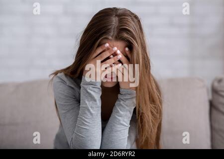 Millennial woman covering her face with hands and crying, feeling depressed or stressed Stock Photo
