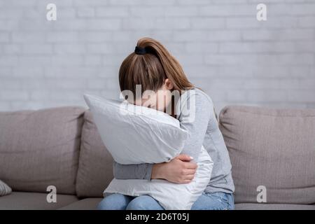 Young woman with depression hugging pillow and crying on sofa at home Stock Photo