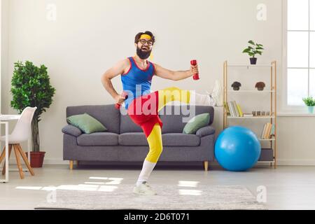 Happy funny young man in retro activewear exercising with dumbbells and laughing Stock Photo