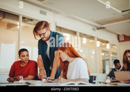 Male teacher assisting teenage students in the classroom. Male professor helping girl students during a class at high school. Stock Photo