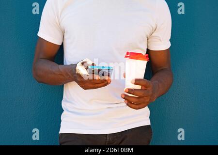Close up of a black man using the phone and with a coffee to go. Takeaway coffee and technology concept. Stock Photo