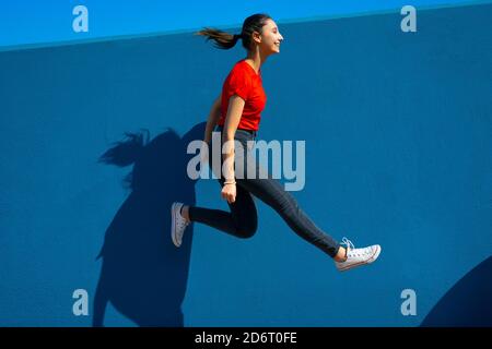 Happy Woman in red dress jumping on a blue background. Woman jumping and having fun. Happiness and joy concept. Stock Photo