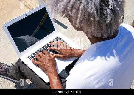 Top view of a black man working on a white laptop. Concept of looking for work and working outdoors. Stock Photo