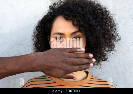 Anonymous African American male friend covering face of young attentive female with Afro hairstyle near cement wall while looking at camera Stock Photo