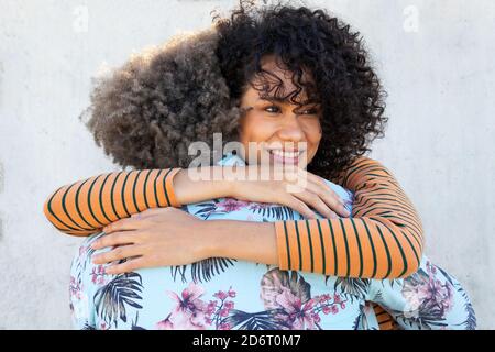 Happy young ethnic female with curly hair smiling and embracing unrecognizable boyfriend while spending time together on street Stock Photo