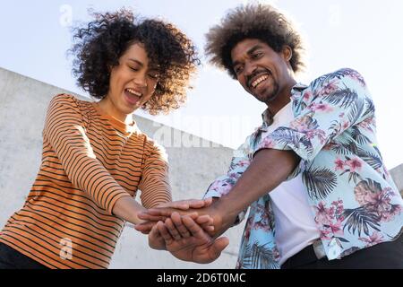From below of positive young African American male and female putting hands together and smiling while having fun on sunny day Stock Photo