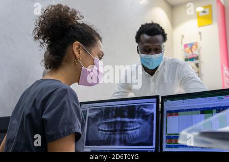 Side view of black female doctor in medical mask examining X ray on monitor of computer while working in modern dental clinic Stock Photo