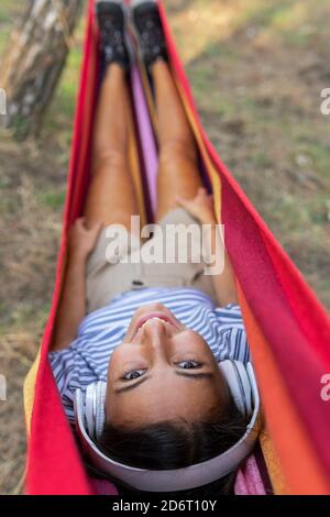 Peaceful female in headphones lying in hammock and enjoying calm music and looking at camera Stock Photo