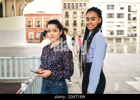 Crop young happy multiracial students with cellphone talking on city street near houses Stock Photo