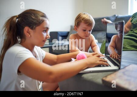Side view of peaceful boy and girl sitting near sofa and using laptop together while choosing cartoon and resting at weekend at home Stock Photo
