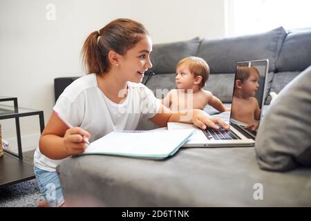 Side view of peaceful boy and girl sitting near sofa and using laptop together while choosing cartoon and resting at weekend at home Stock Photo