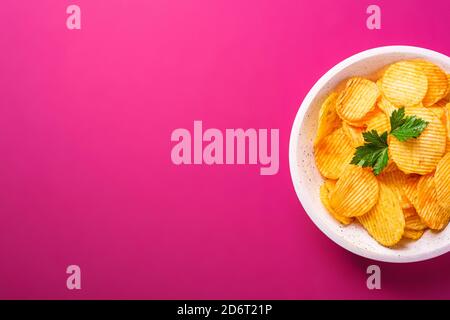 Fried corrugated golden potato chips with parsley leaf in wooden bowl on pink background, top view copy space Stock Photo