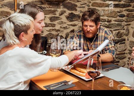 Group of friends gathering at table in restaurant and discussing menu while getting ready for ordering food for dinner Stock Photo