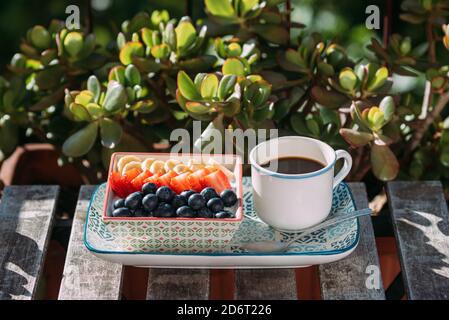 Appetizing breakfast with various fruits and berries arranged on wooden table with cup of aromatic coffee in outdoors cafe Stock Photo