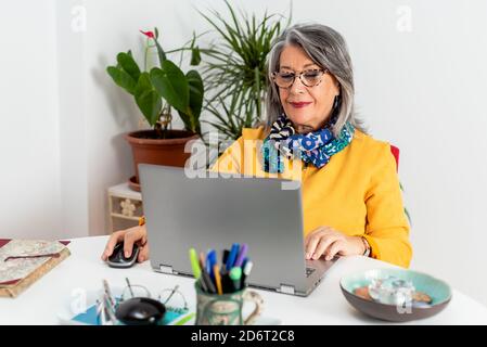 Content respectable mature businessWoman wearing trendy elegant clothes and eyeglasses browsing modern netbook in light office Stock Photo