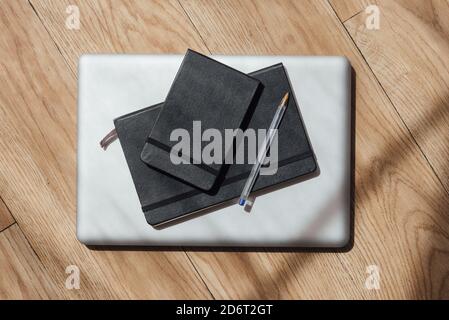 Top view composition of notepads in black cover arranged with pen on contemporary netbook on parquet Stock Photo