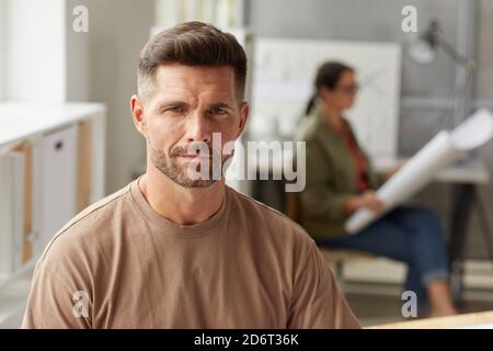 Portrait of mature bearded architect looking camera and smiling while sitting at drawing desk in sunlight, copy space Stock Photo